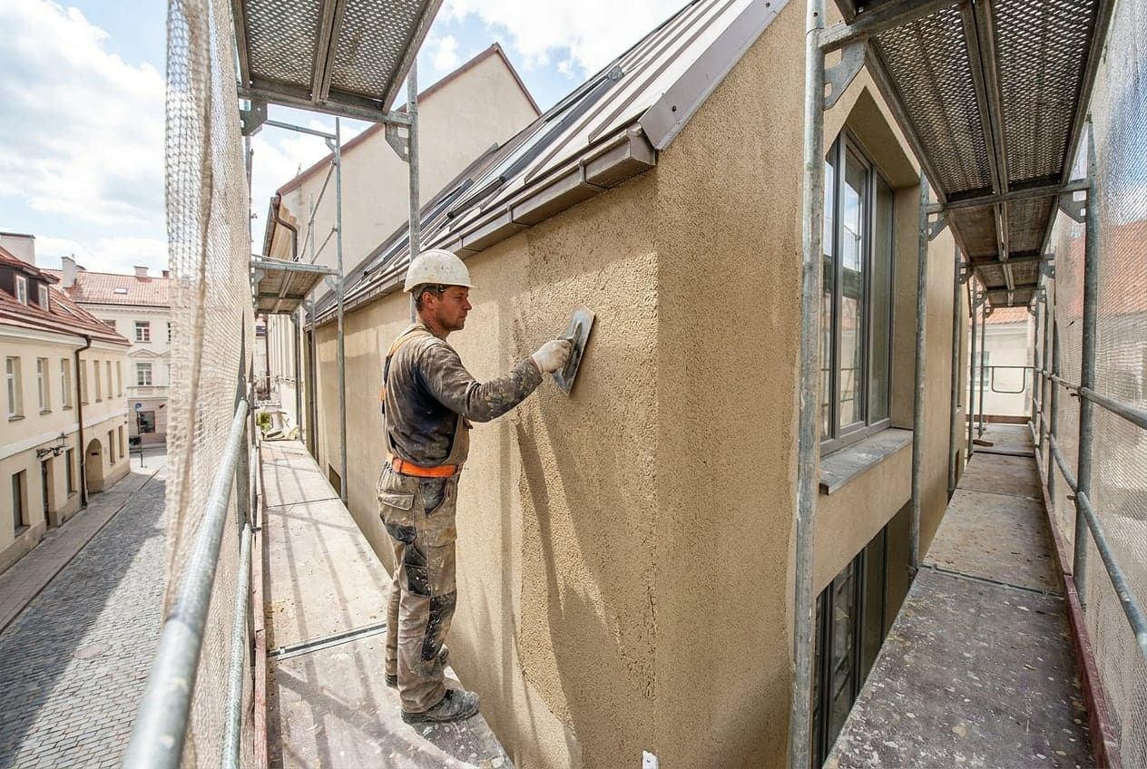 Darbininkas ant pastolių užneša dekoratyvinį tinką ant apšiltinto fasado Vilniuje